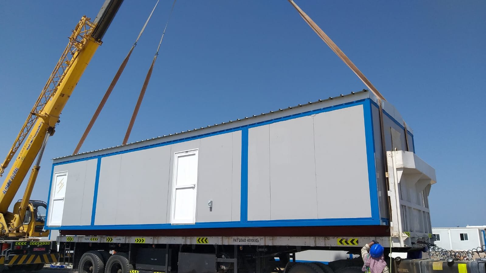 Porta cabin with door being lifted by crane onto a delivery truck