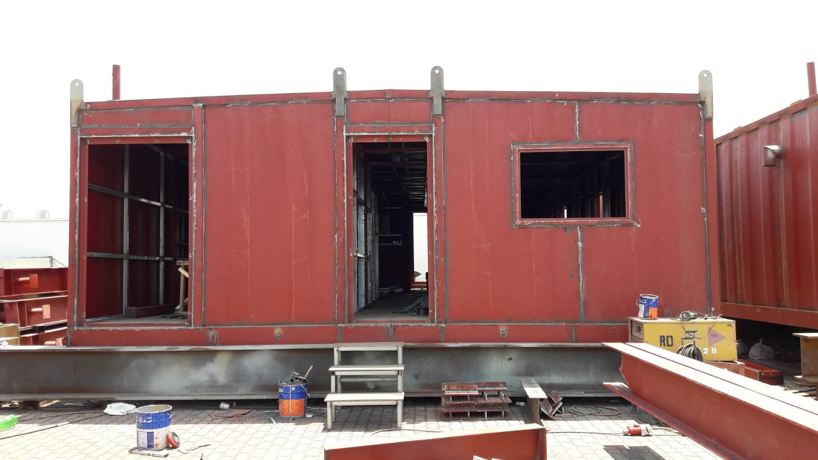 Red steel cabin with door and window openings during fabrication